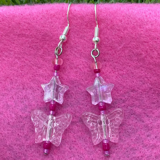 Butterfly-shaped earrings on silver hooks with pink beads on a pink surface.