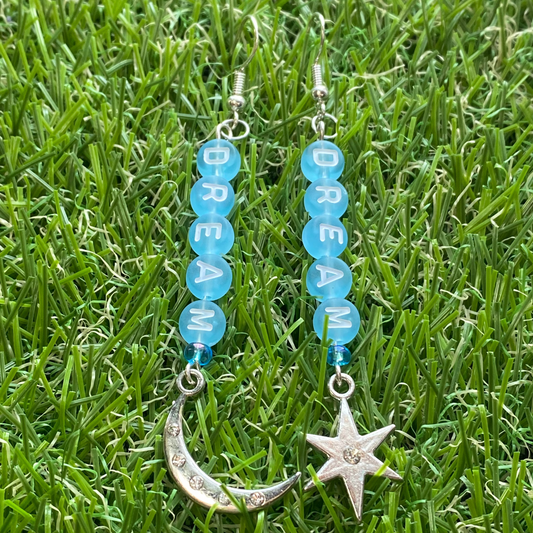 Pair of earrings with blue beads spelling the word dream and star and moon charms on grass