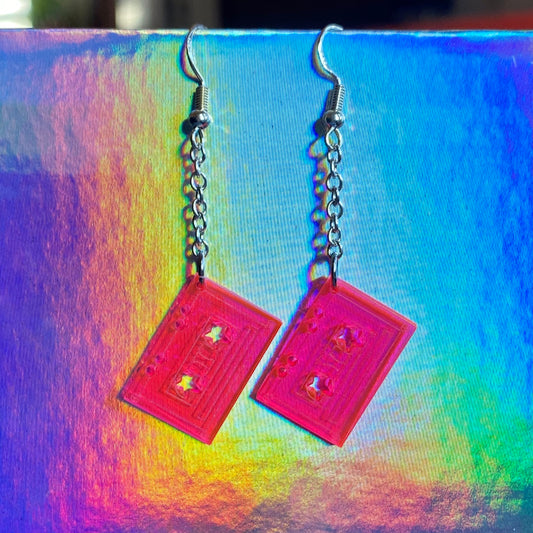 Pink acrylic cassette tape shaped earrings with star designs on a colorful background