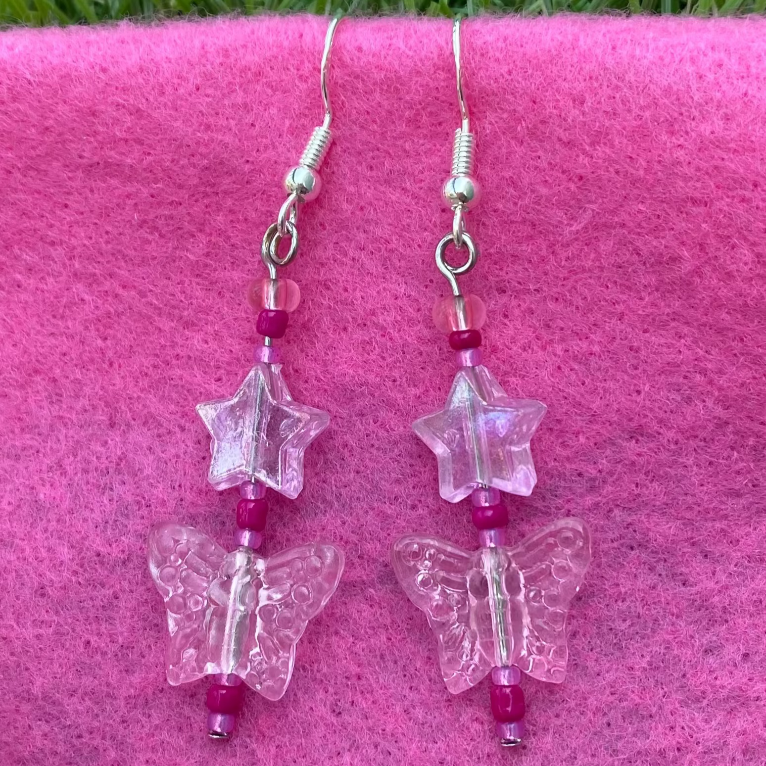 Butterfly-shaped earrings on silver hooks with pink beads on a pink surface.