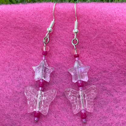 Butterfly-shaped earrings on silver hooks with pink beads on a pink surface.