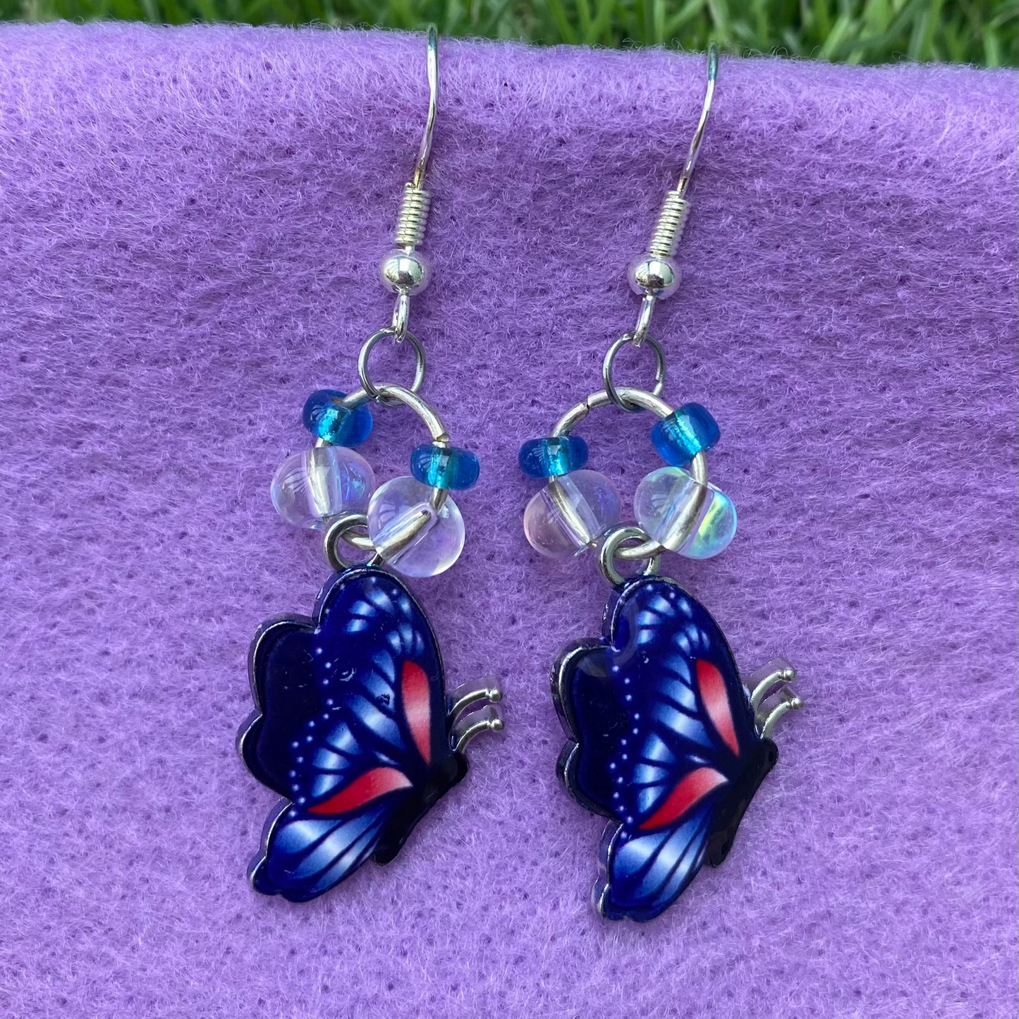 Butterfly-shaped earrings on a purple surface with grass in the background