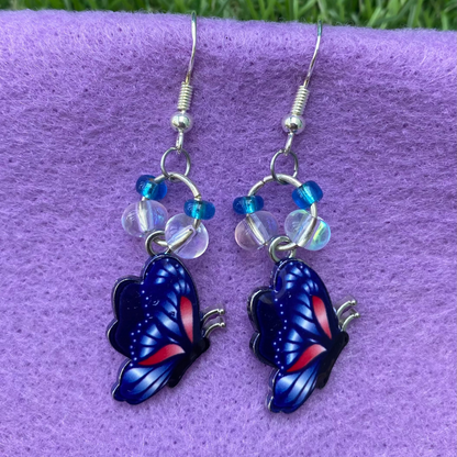 Butterfly-shaped earrings on a purple surface with grass in the background