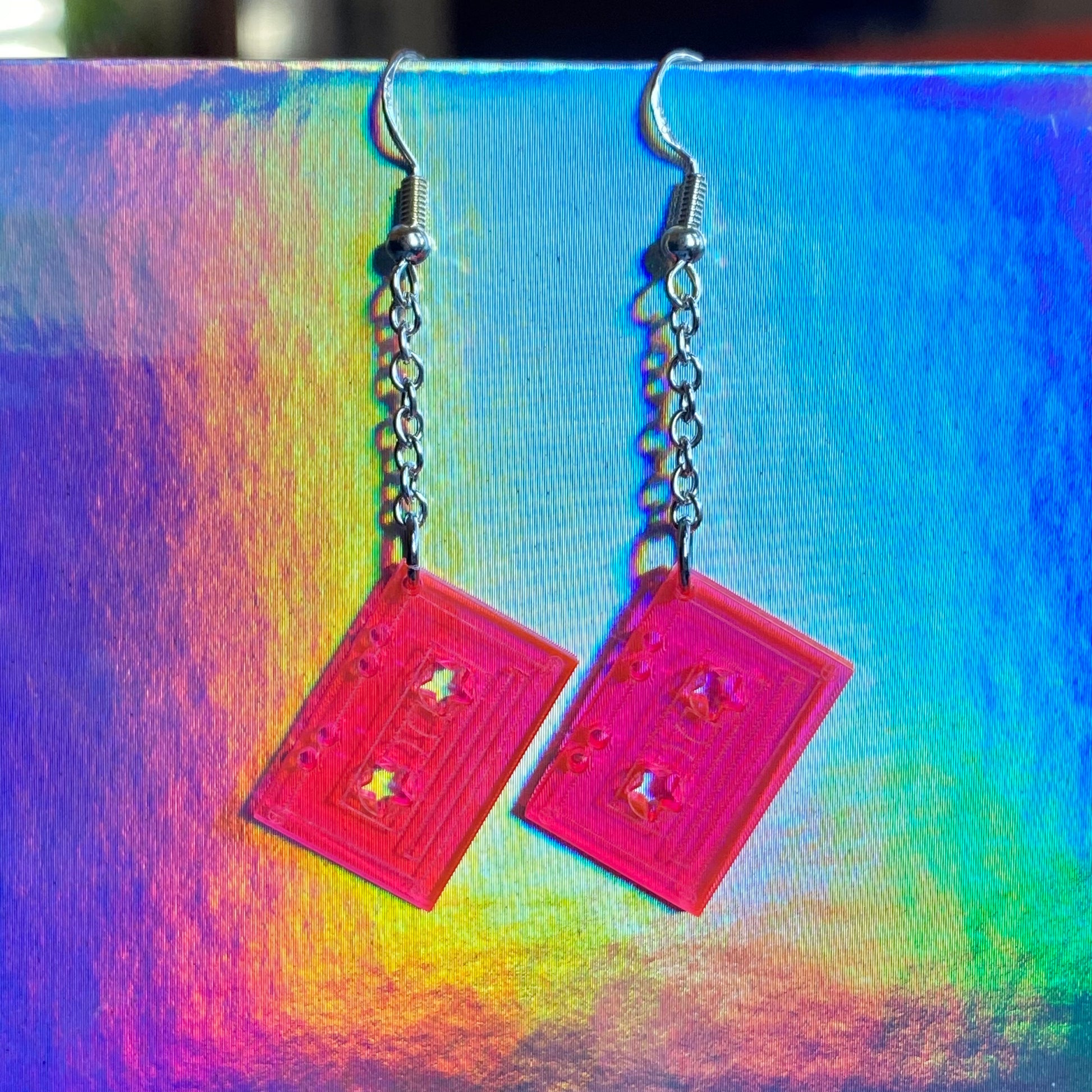 Pink acrylic cassette tape shaped earrings with star designs on a colorful background
