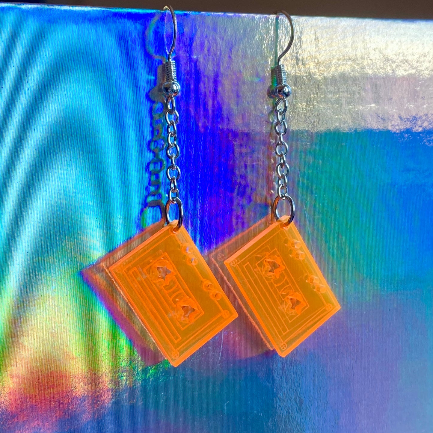 Pair of earrings with orange cassette-shaped pendants on a colorful background