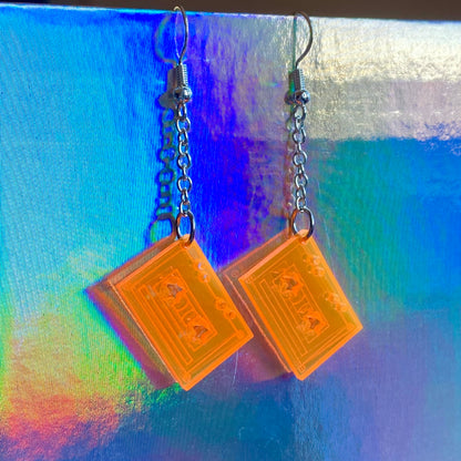 Pair of earrings with orange cassette-shaped pendants on a colorful background